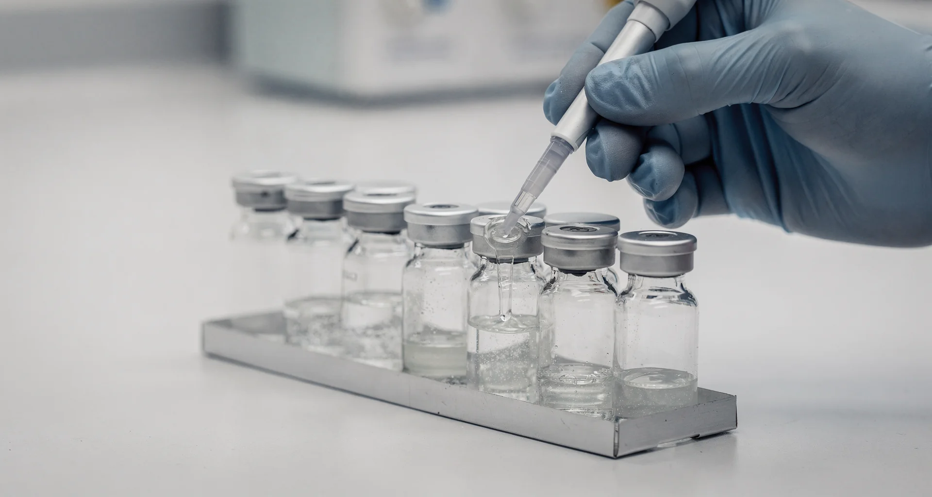 Precision laboratory benchwork showing micropipette and glass vials during batch preparation.